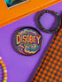 Round black pinback button with neon embroidery-style waves surrounding bold yellow and red "DISOBEY" text.